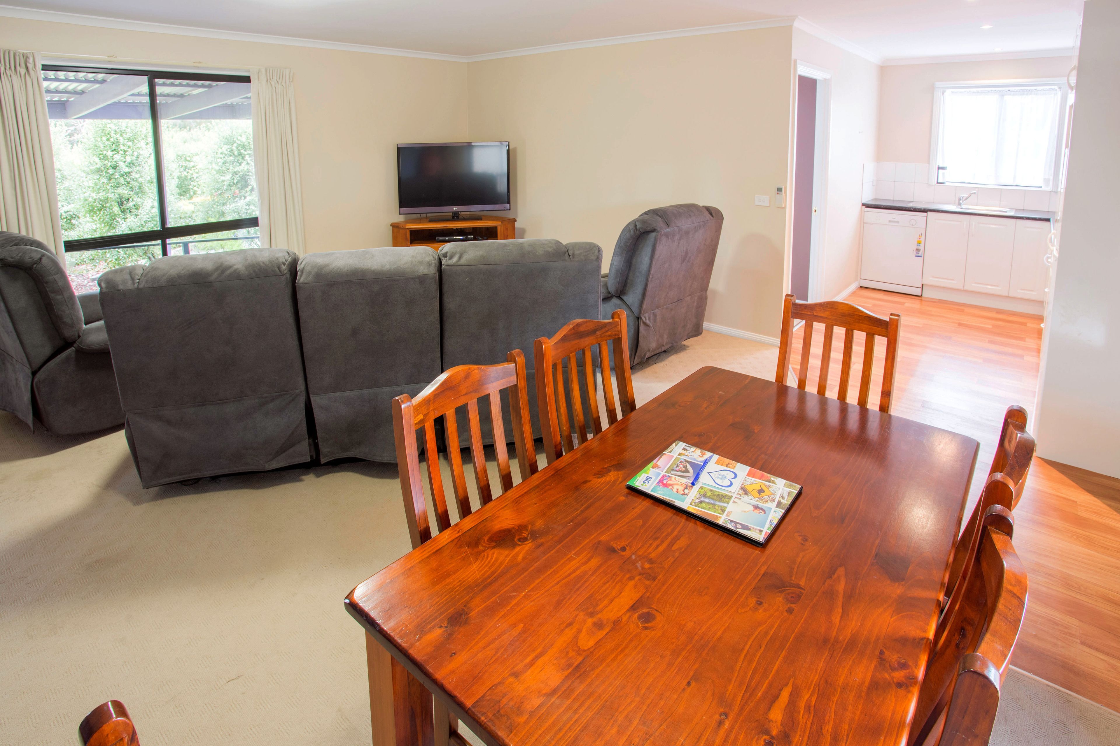 A living room with a wooden dining table, grey sofa, and a television.