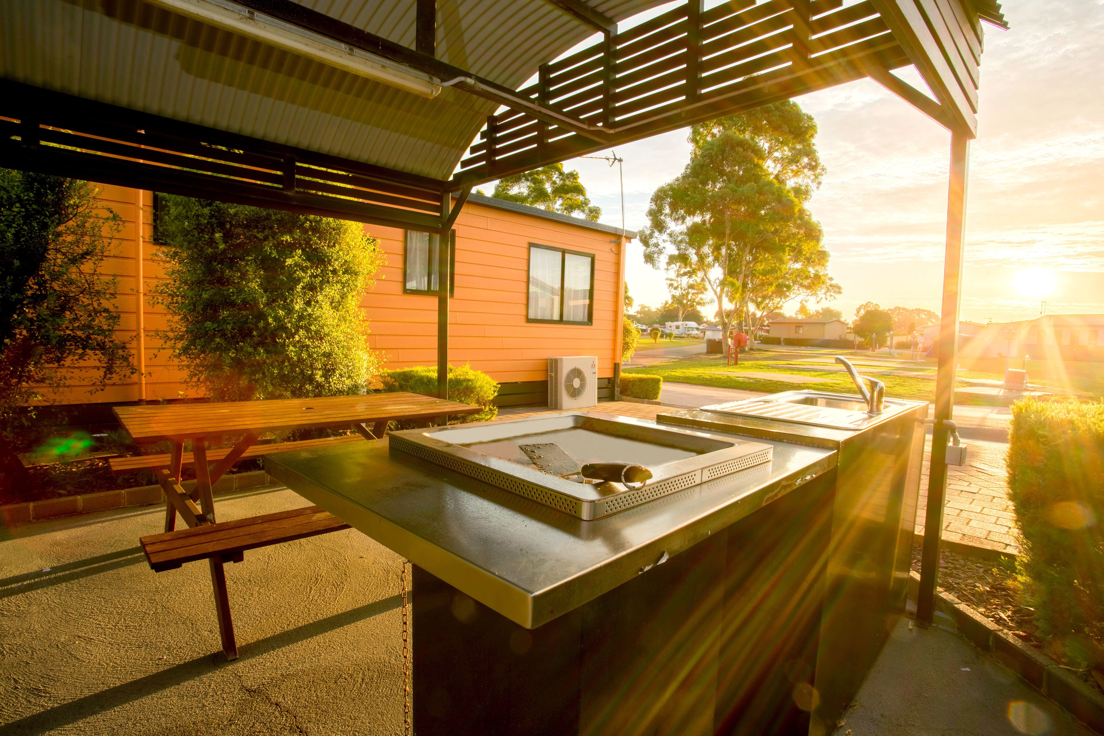 Un área de cocina al aire libre con una parrilla, un lavamanos y una mesa de picnic de madera.