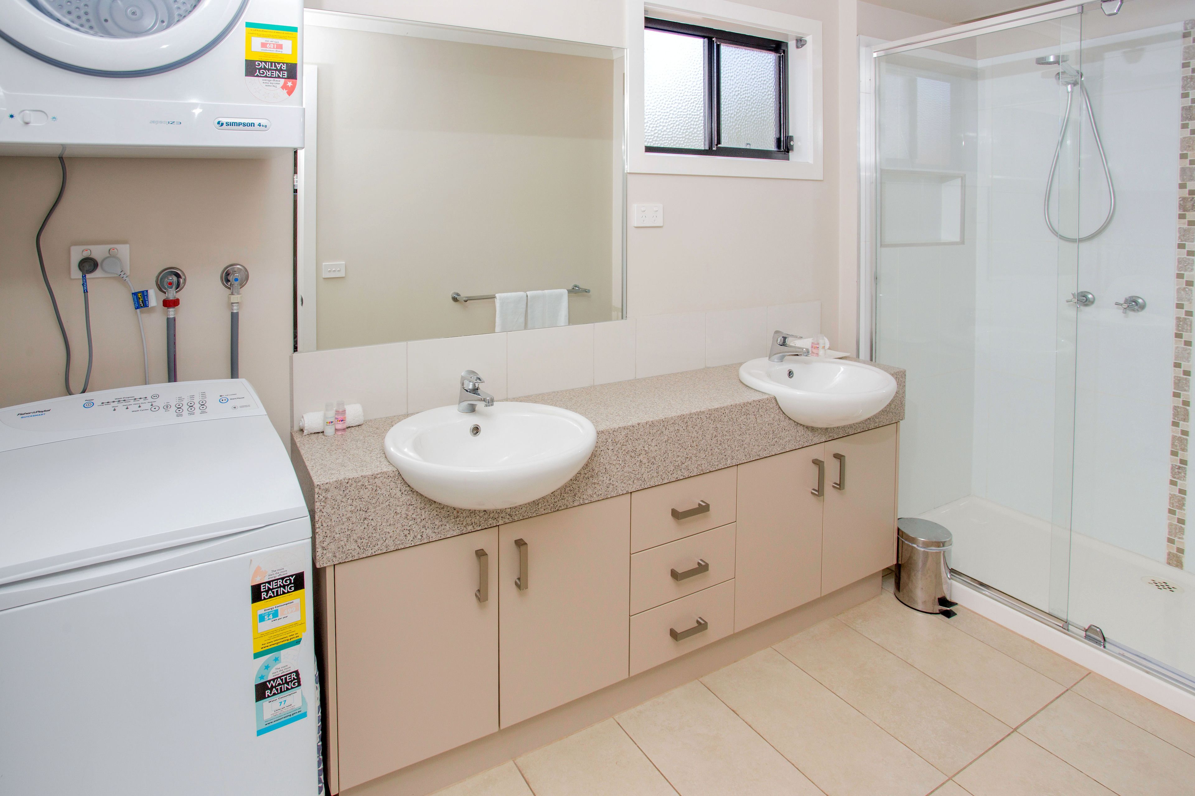 Un baño con dos lavamanos, una lavadora y cabina de ducha de vidrio.