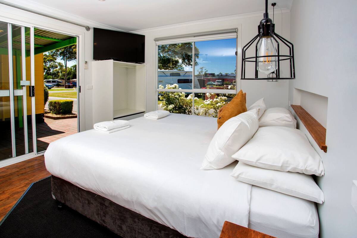 Een moderne slaapkamer met een groot bed, een schuifdeur naar een buitenruimte en een aan de muur bevestigde televisie.