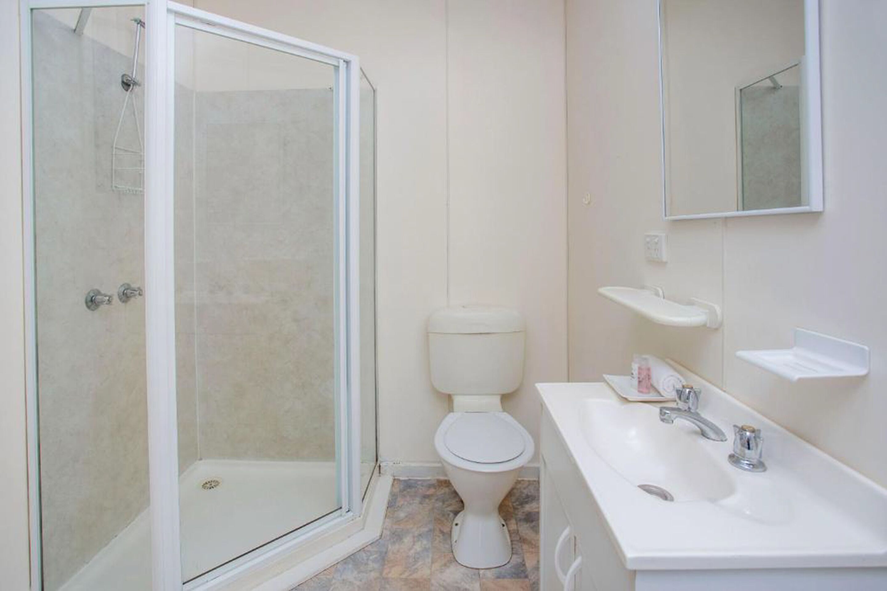 A bathroom with a glass-enclosed shower, a toilet, and a sink with a mirror above it.