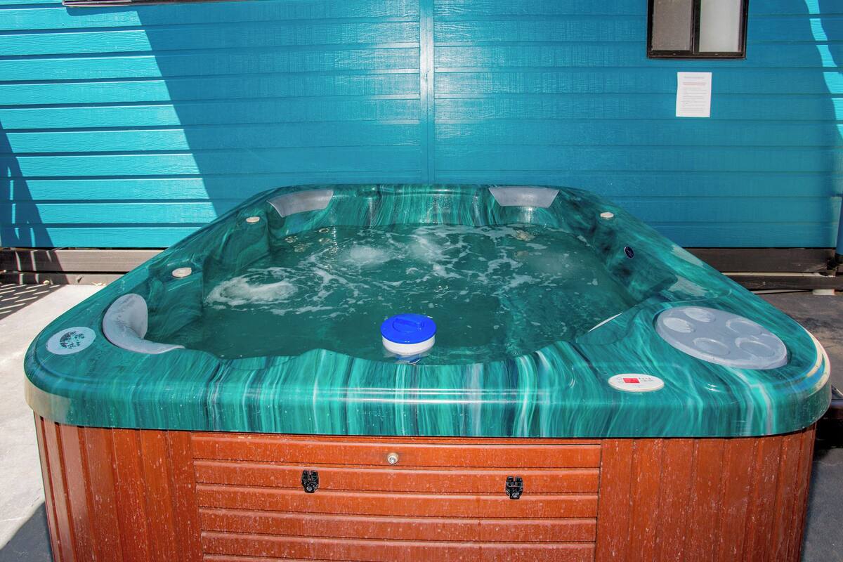 Een hottub met een blauwe buitenkant en een houten onderstel, buiten geplaatst tegen een blauw gebouw.