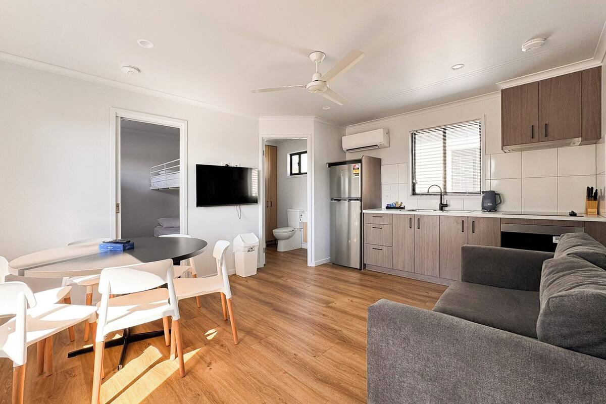 Een moderne keuken met een ingebouwde oven, een koelkast en een spoelbak. Er is een eethoek met een tafel en stoelen.