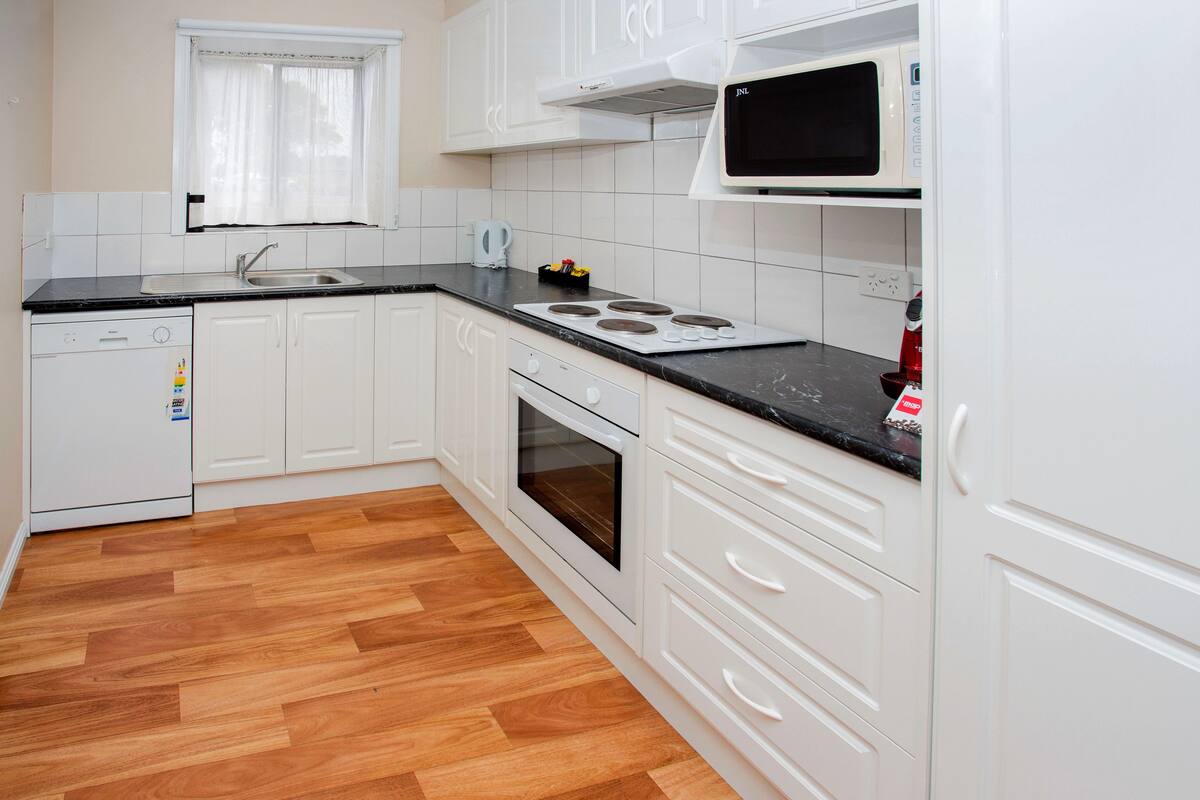 Een keuken met witte kastjes, een zwart aanrecht, een magnetron, een fornuis en een vaatwasser.