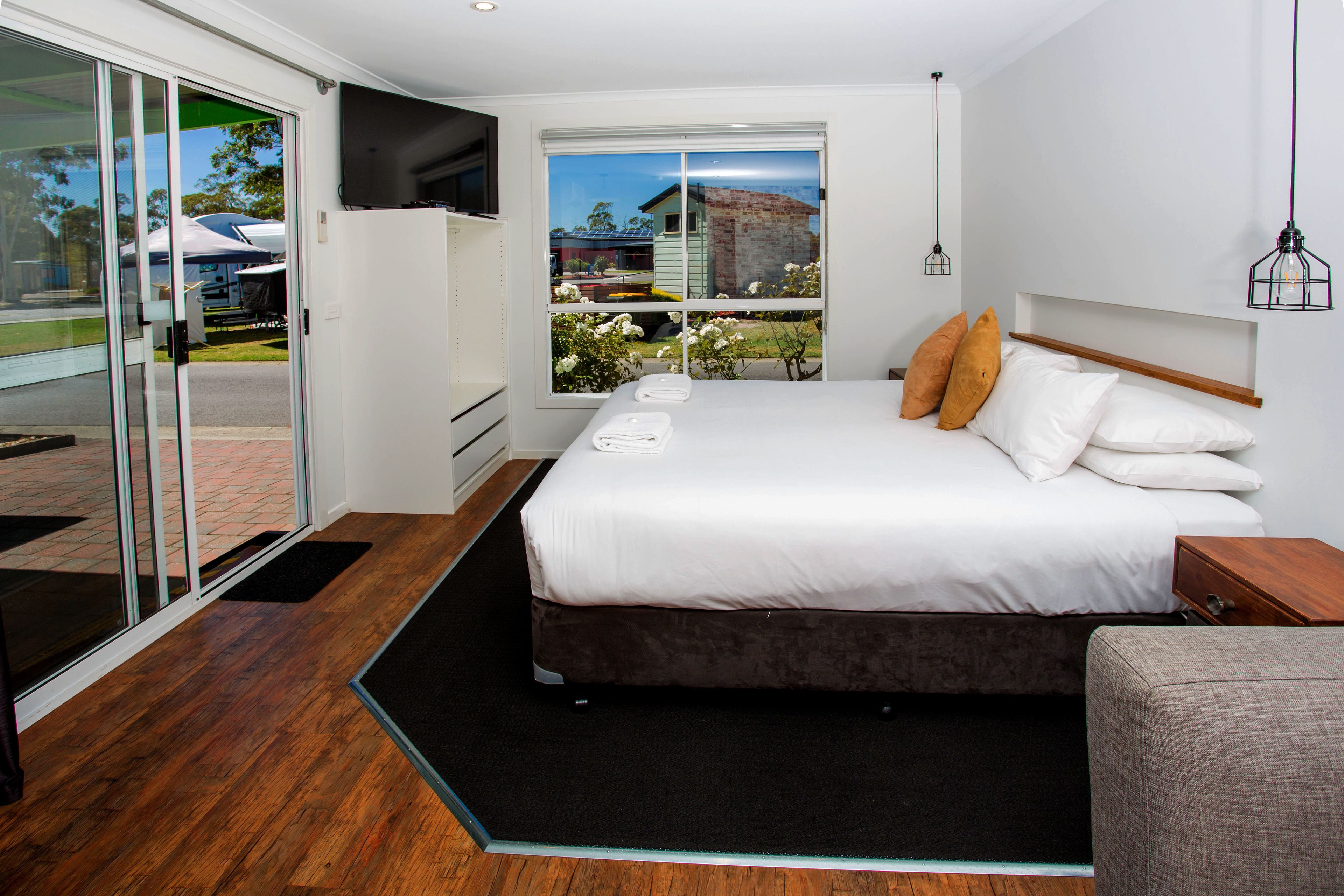 A modern bedroom with a large bed, a TV mounted on the wall, and a view of the outdoors through a sliding door.