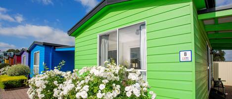Una casa móvil verde con un letrero con el número 8, flores blancas al frente y un cielo azul despejado.