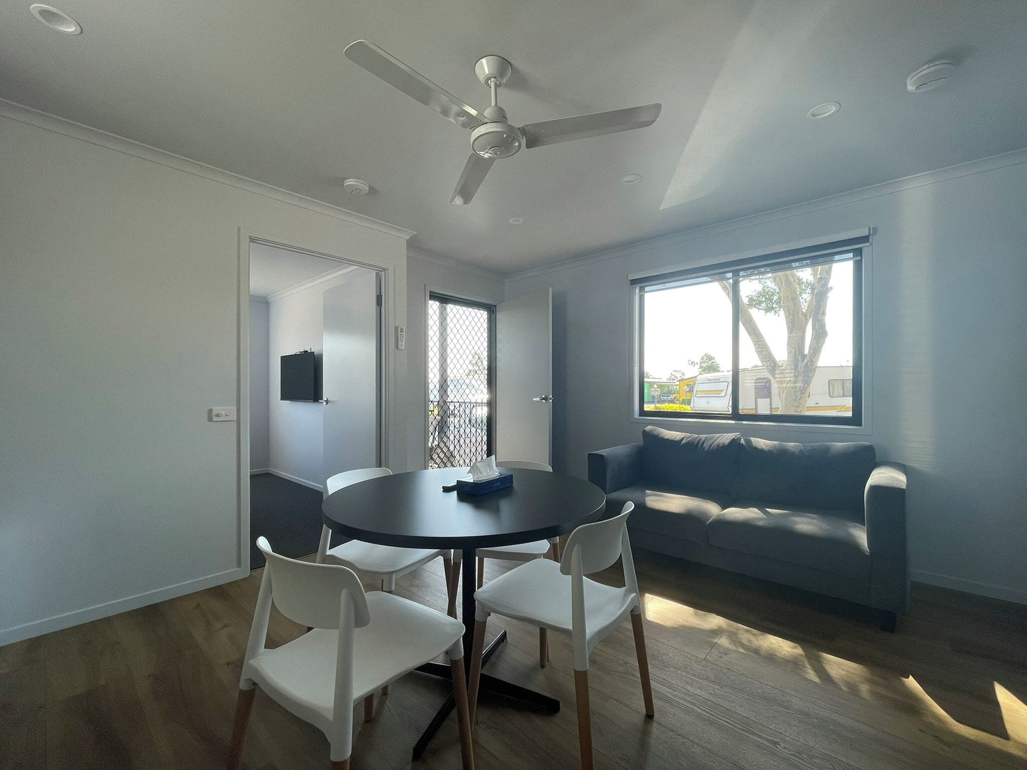 A modern living room with a round table, white chairs, a grey sofa, and a ceiling fan.