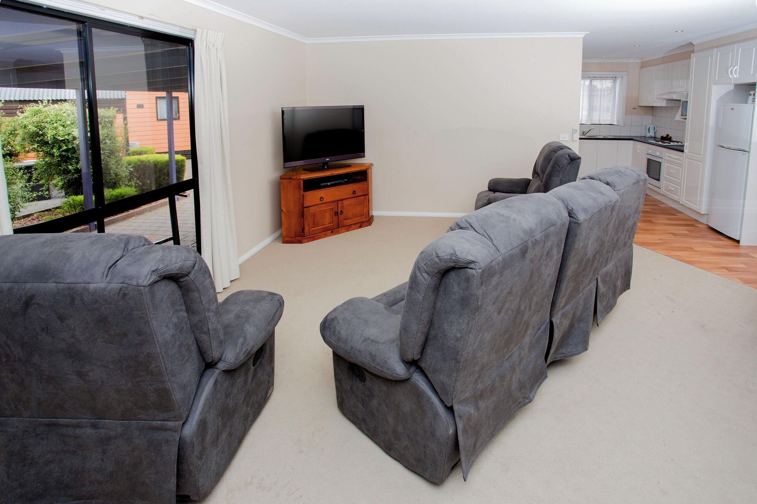 A modern living room with grey sofas, a flat-screen TV on a wooden stand, and a large sliding glass door leading to a balcony.