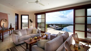 A spacious living room with a large sofa, a coffee table, and a view of a balcony with a pool. - Villa Ali Agung (Pecatu)