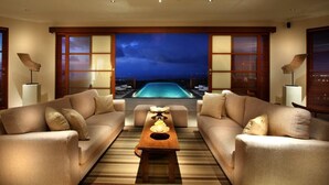 A modern living room with two sofas facing a pool, a coffee table, and large windows with a view of the pool at night. - Villa Ali Agung (Pecatu)