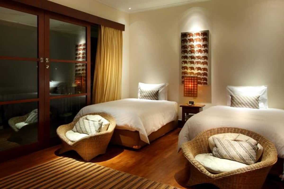 A hotel room with two beds, wicker chairs, a large sliding glass door, and a wall-mounted light fixture.