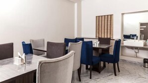 A modern hotel room with a dining area featuring a marble table and chairs, a large mirror, and a wooden accent wall. - Simi International - The Imperial (Bidhannagar)