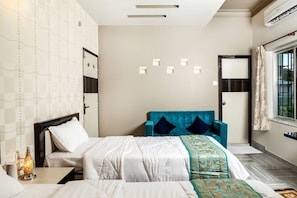 Una habitación de hotel con cama, mesita de noche, lámpara de pared, ventana con cortinas y una puerta.