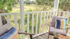 A wooden deck with two cushioned chairs and a small table, surrounded by white railings. - Clonmara Country House & Cottages (Port Fairy)