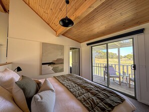 A bedroom with a bed, a painting, a desk, and a view through a sliding door to an outdoor deck.