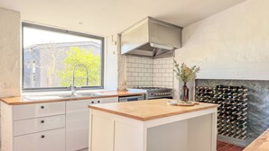 A modern kitchen with a window, white cabinetry, a built-in stove, and a wine rack. - Clonmara Country House & Cottages (Port Fairy)