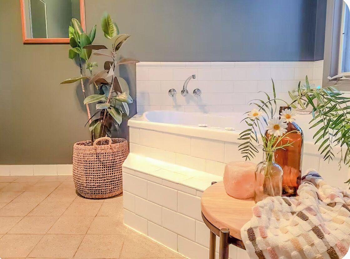 A bathroom with a white bathtub, a woven basket, and potted plants.