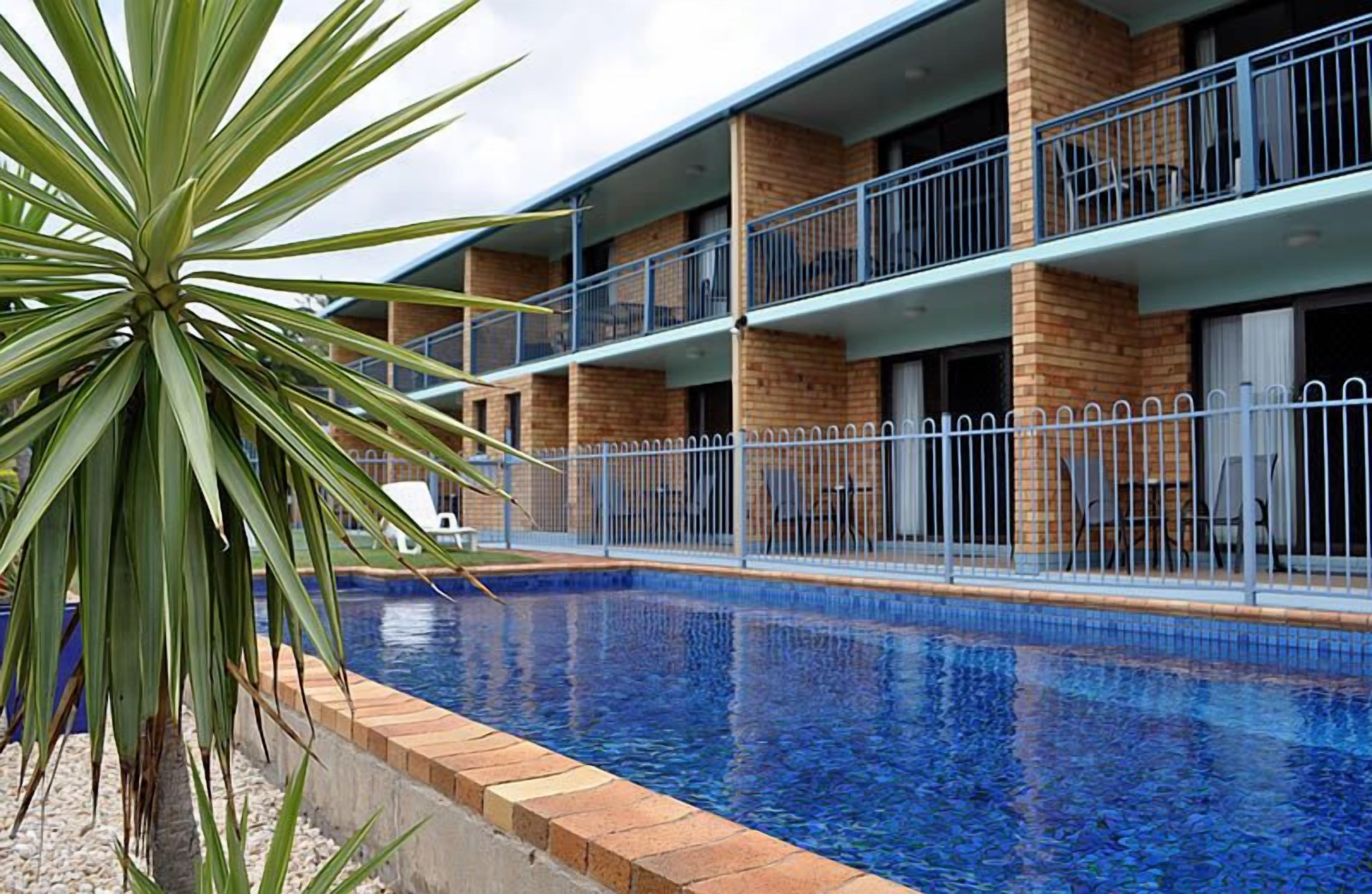 Ein mehrstöckiges Hotel mit Schwimmbad, Balkonen und einer Palme.