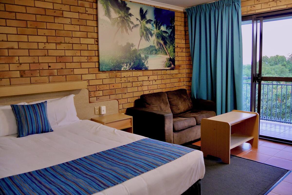 Une chambre d’hôtel avec un grand lit, un canapé, une petite table et un balcon donnant sur un paysage verdoyant.