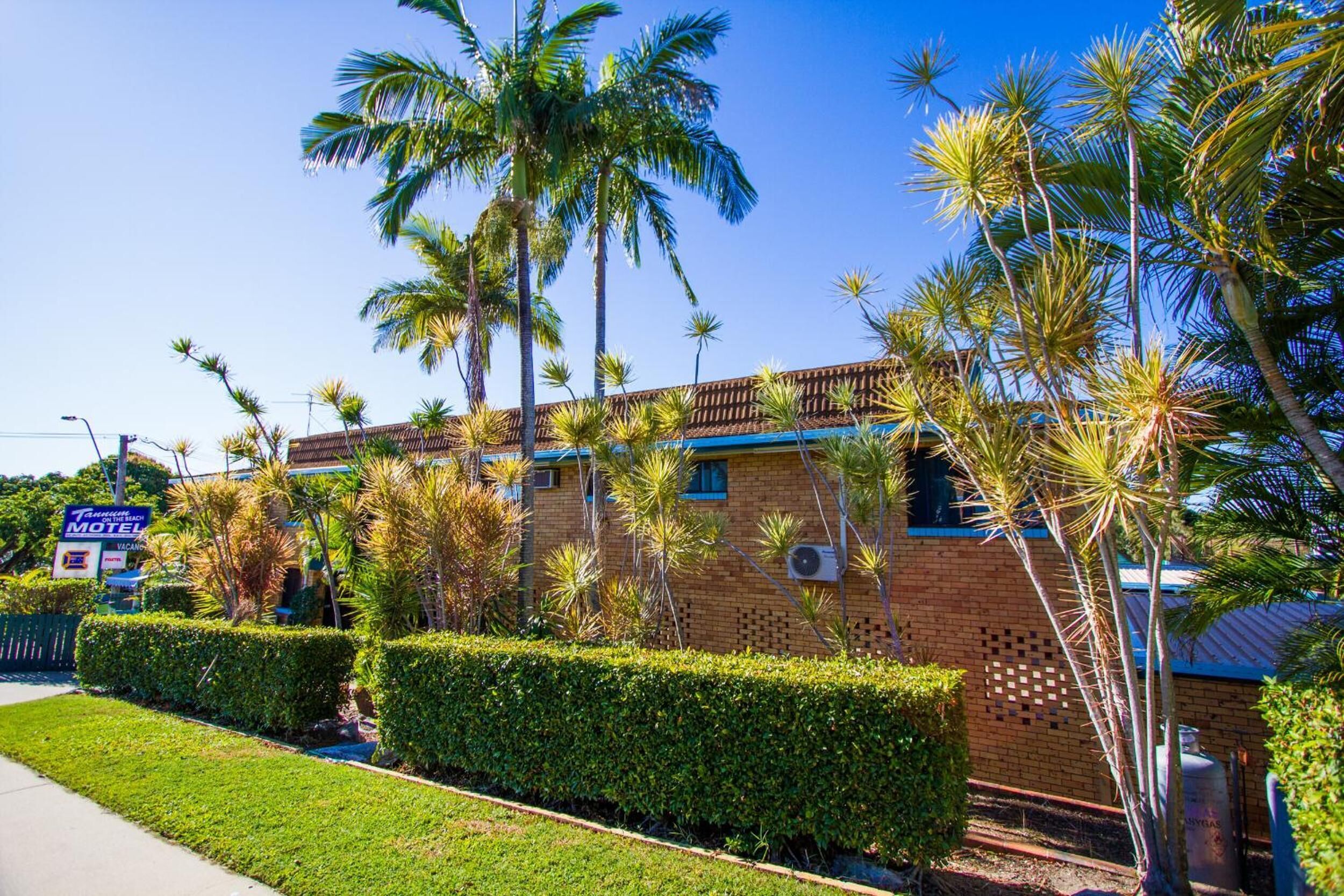 A motel with a brick exterior, palm trees, and a well-maintained lawn.