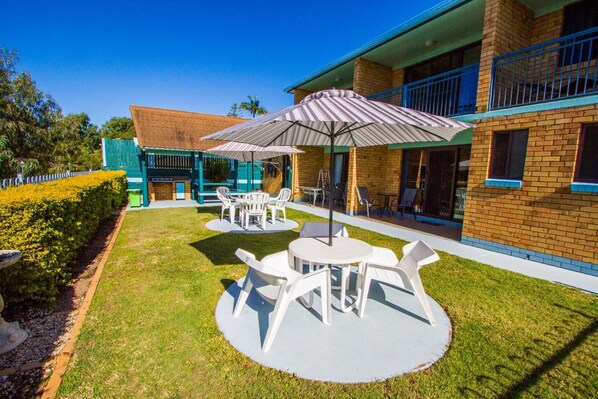 A courtyard with outdoor seating, a pool, and a building with a brick facade and blue accents. - Tannum on the Beach Motel (Tannum Sands)