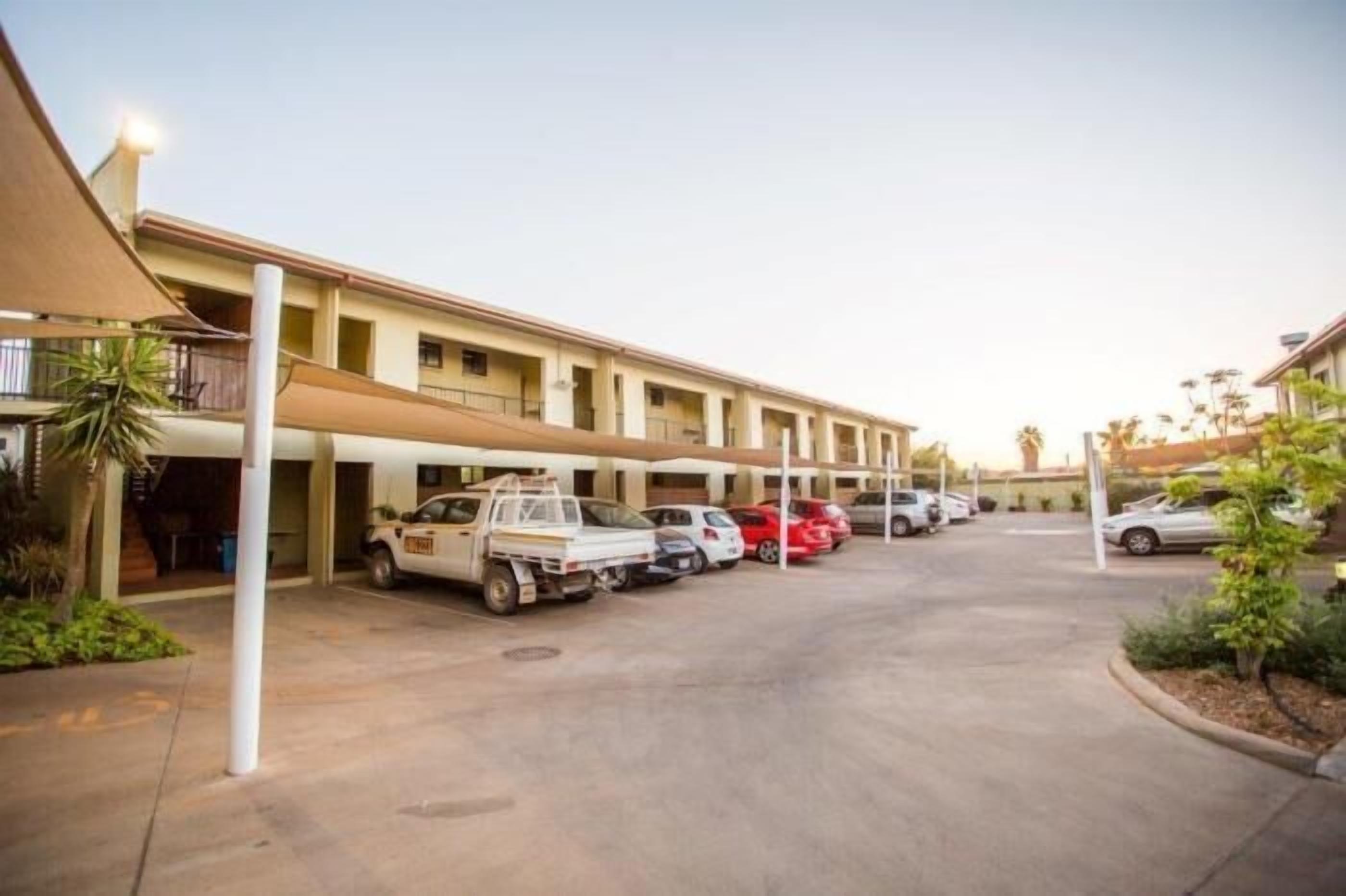 A motel with a parking lot, a white pickup truck, and several cars parked in front.