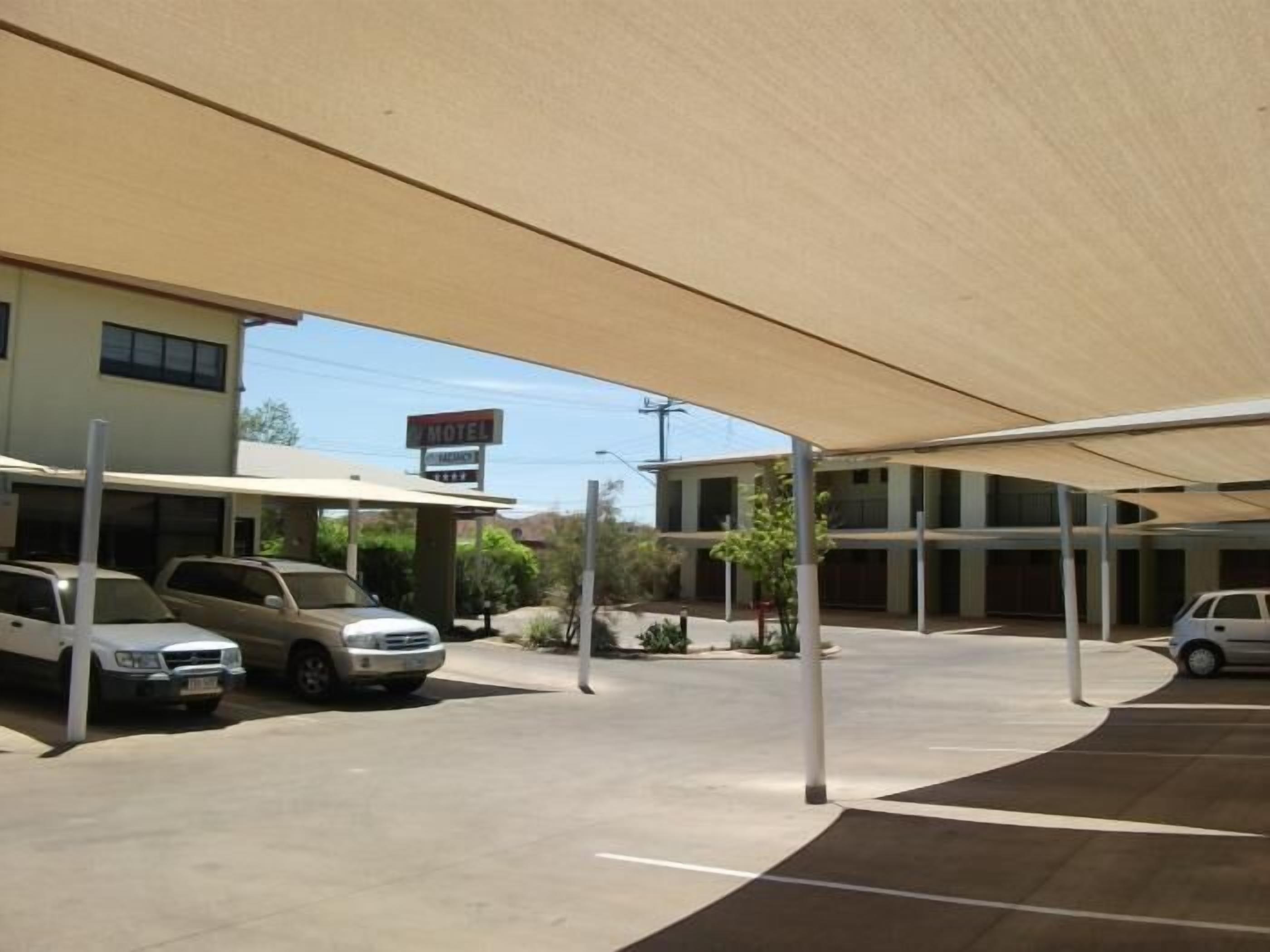 A motel with a covered parking area, a signboard, and a building with a flat roof.
