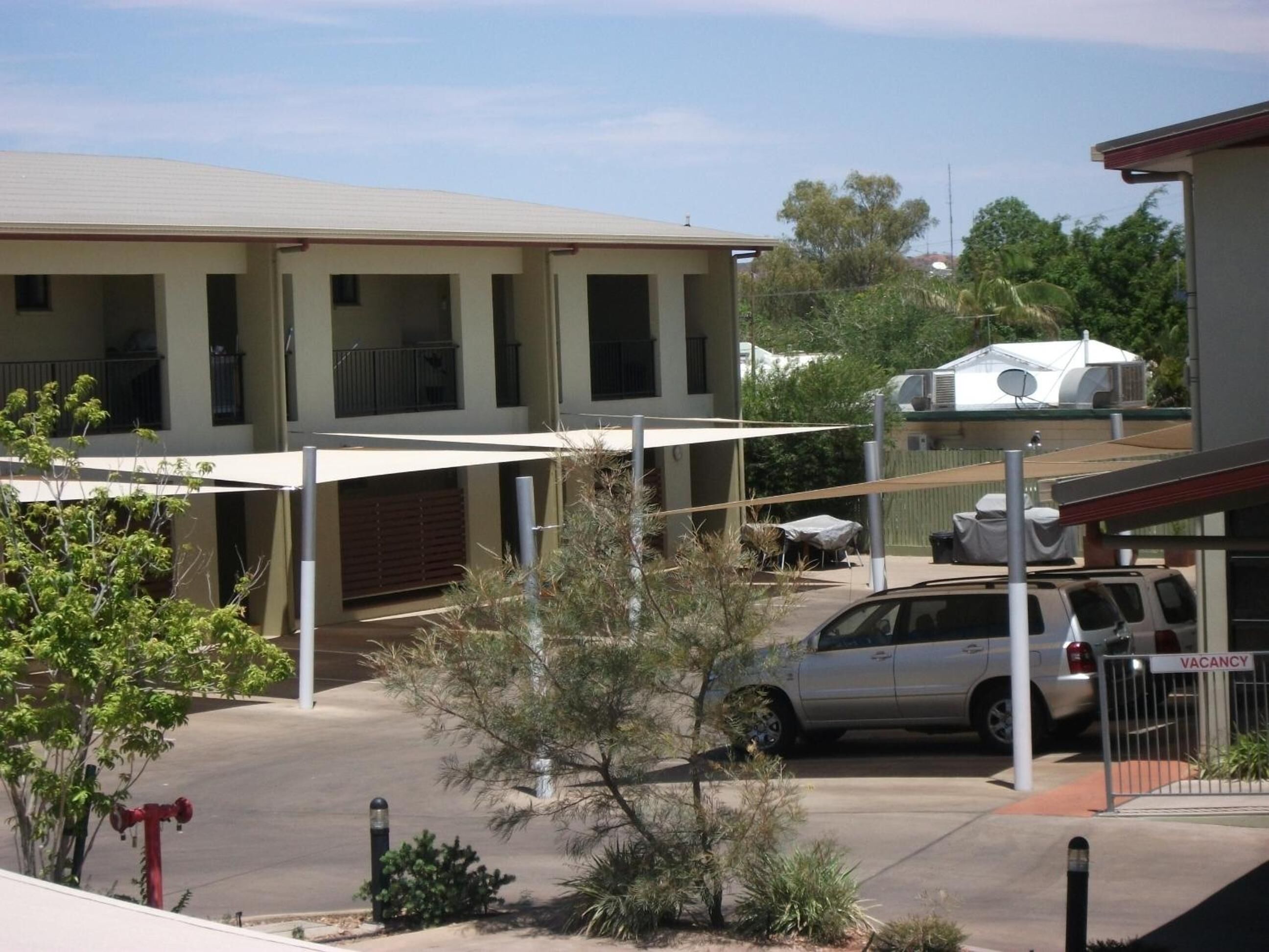 Un edificio de varios pisos con balcones, una zona de estacionamiento techada y una caravana visible.