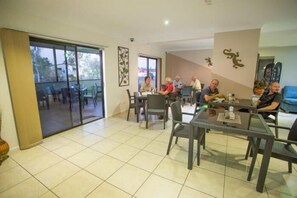 A dining area with tables and chairs, a glass door leading outside, and a wall with decorative elements. - Spinifex Motel & Serviced Apartments (Townview)