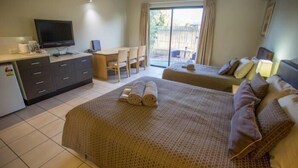 A hotel room with a bed, a desk, a television, and a sliding glass door to an outdoor area. - Spinifex Motel & Serviced Apartments (Townview)