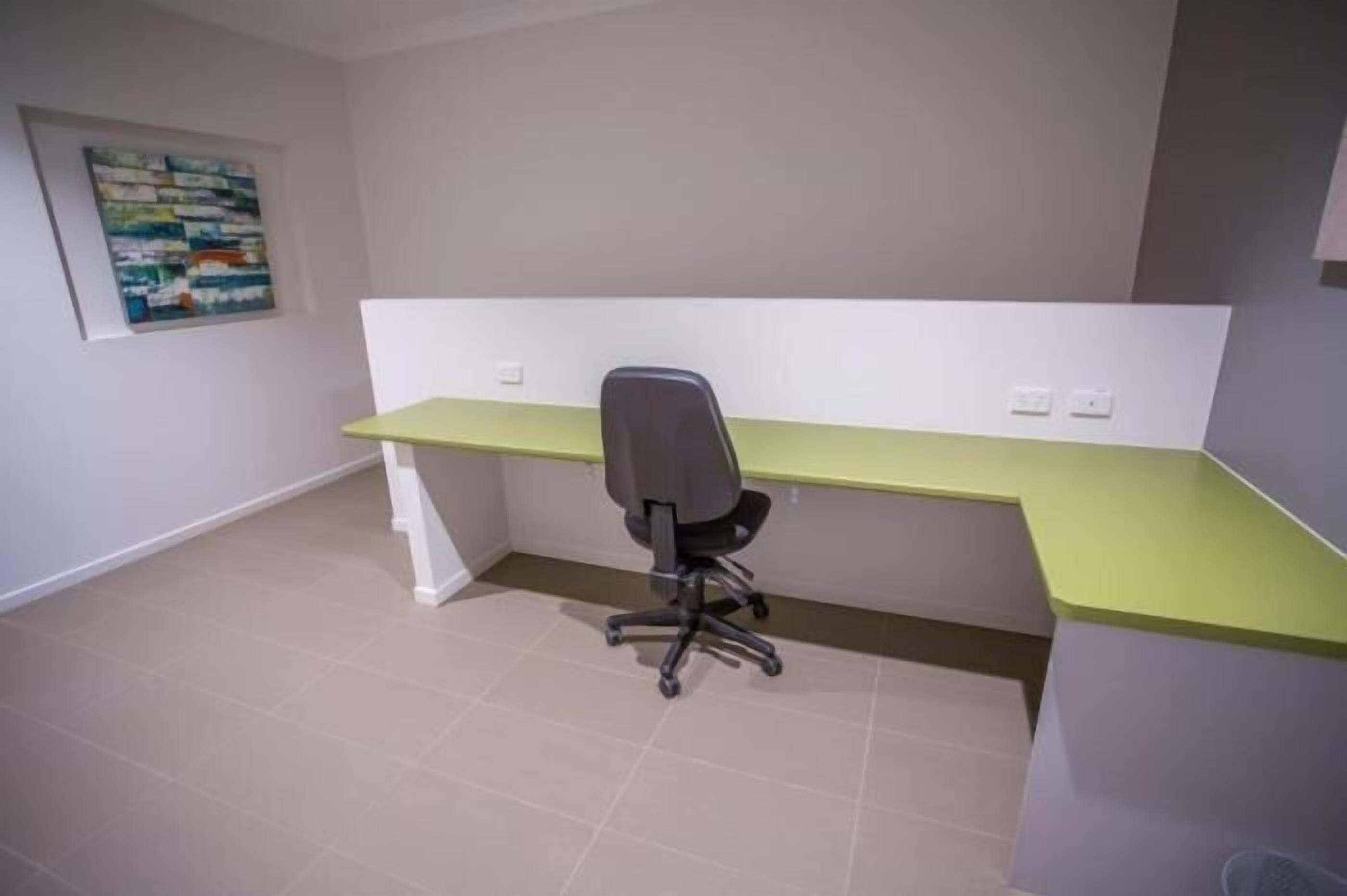 A room with a desk and chair, a white accent wall, and a painting.