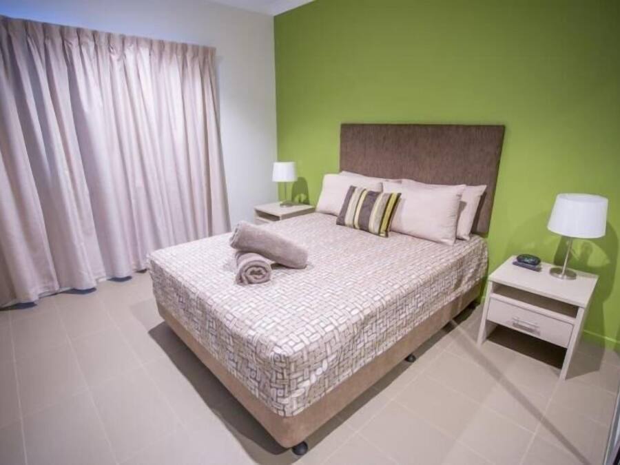 A neatly made bed with a patterned bedspread, two bedside tables with lamps, and a green accent wall.