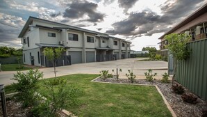 A multi-story residential building with a flat roof, a covered driveway, and a well-maintained lawn with small trees and shrubs. - Spinifex Motel & Serviced Apartments (Townview)