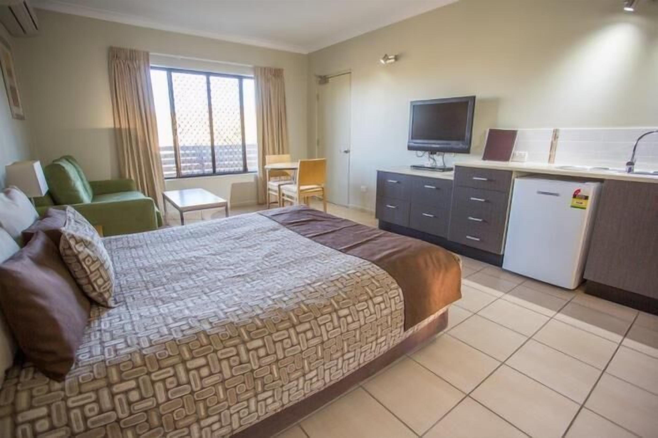 Habitación de hotel con cama, escritorio, silla, televisión y una pequeña cocina.
