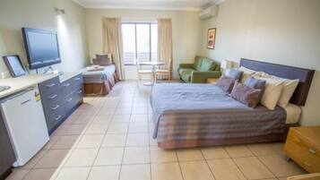 A hotel room with a bed, a desk, a television, and a view of the outside.