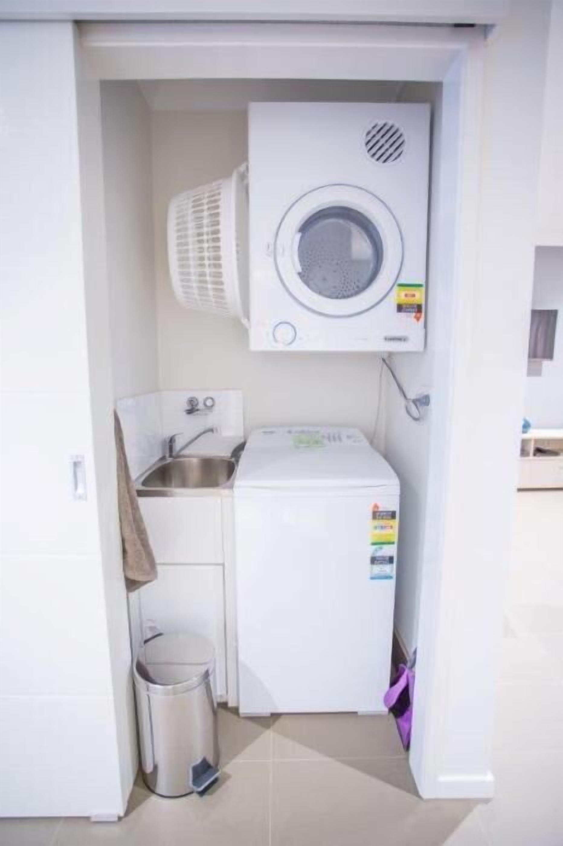 A compact laundry area with a washing machine, a drying machine, a sink, and a trash bin.