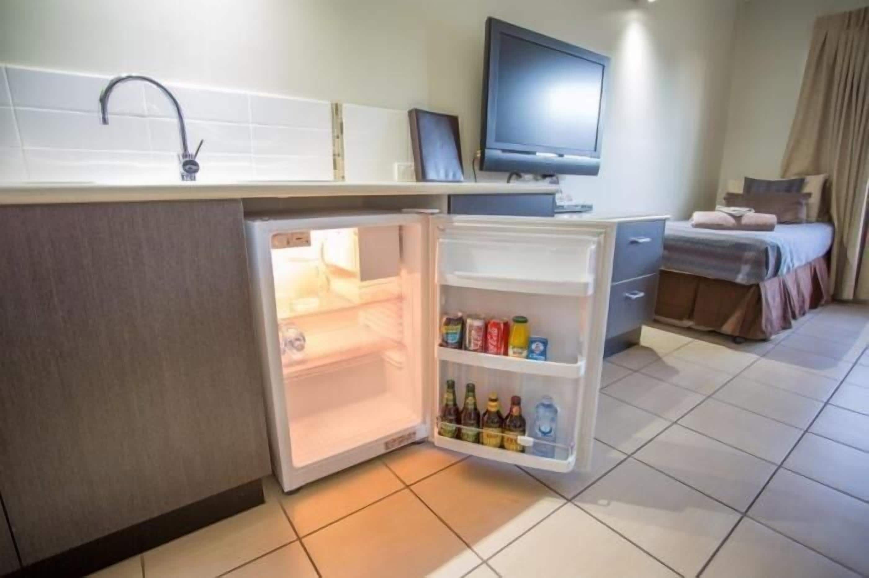 A compact hotel room with a kitchenette, a bed, a television, and a bathroom.