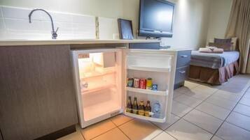 A compact hotel room with a kitchenette, a bed, a television, and a bathroom.