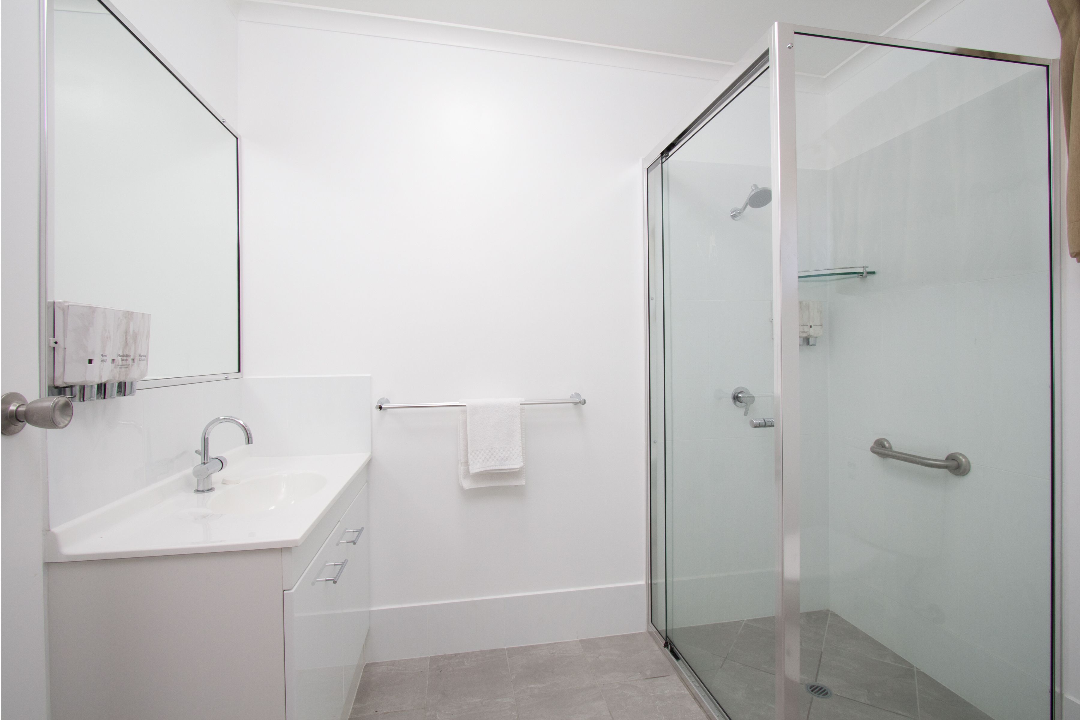 A modern bathroom with a glass-enclosed shower, a white sink, and a towel rack.