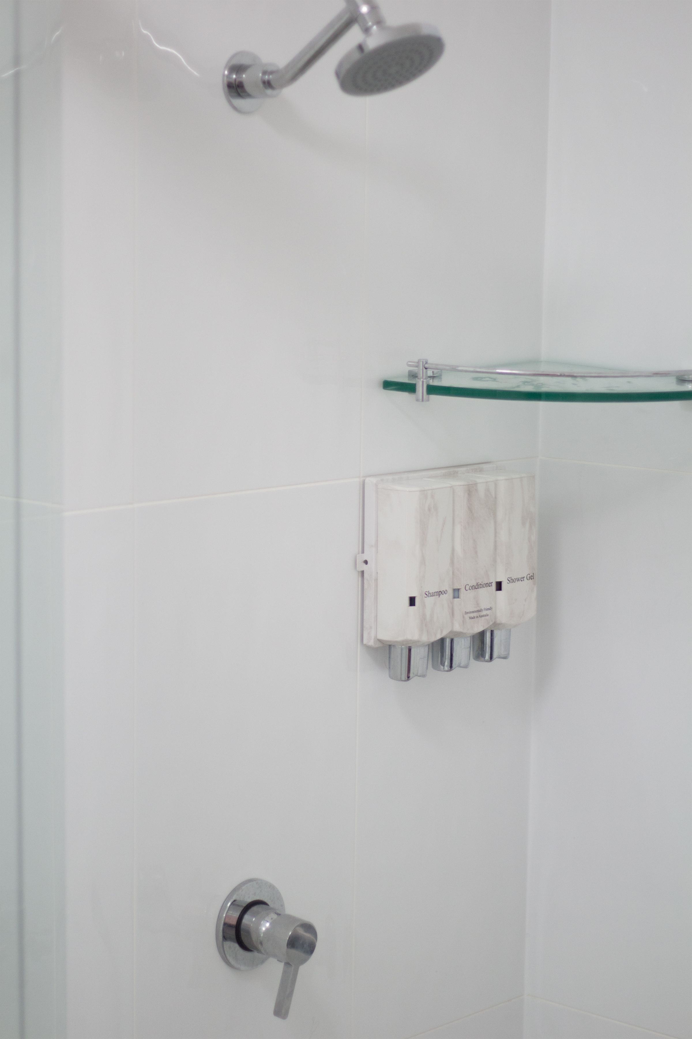 Une salle de bain avec une douche, une étagère en verre et un distributeur de savon.