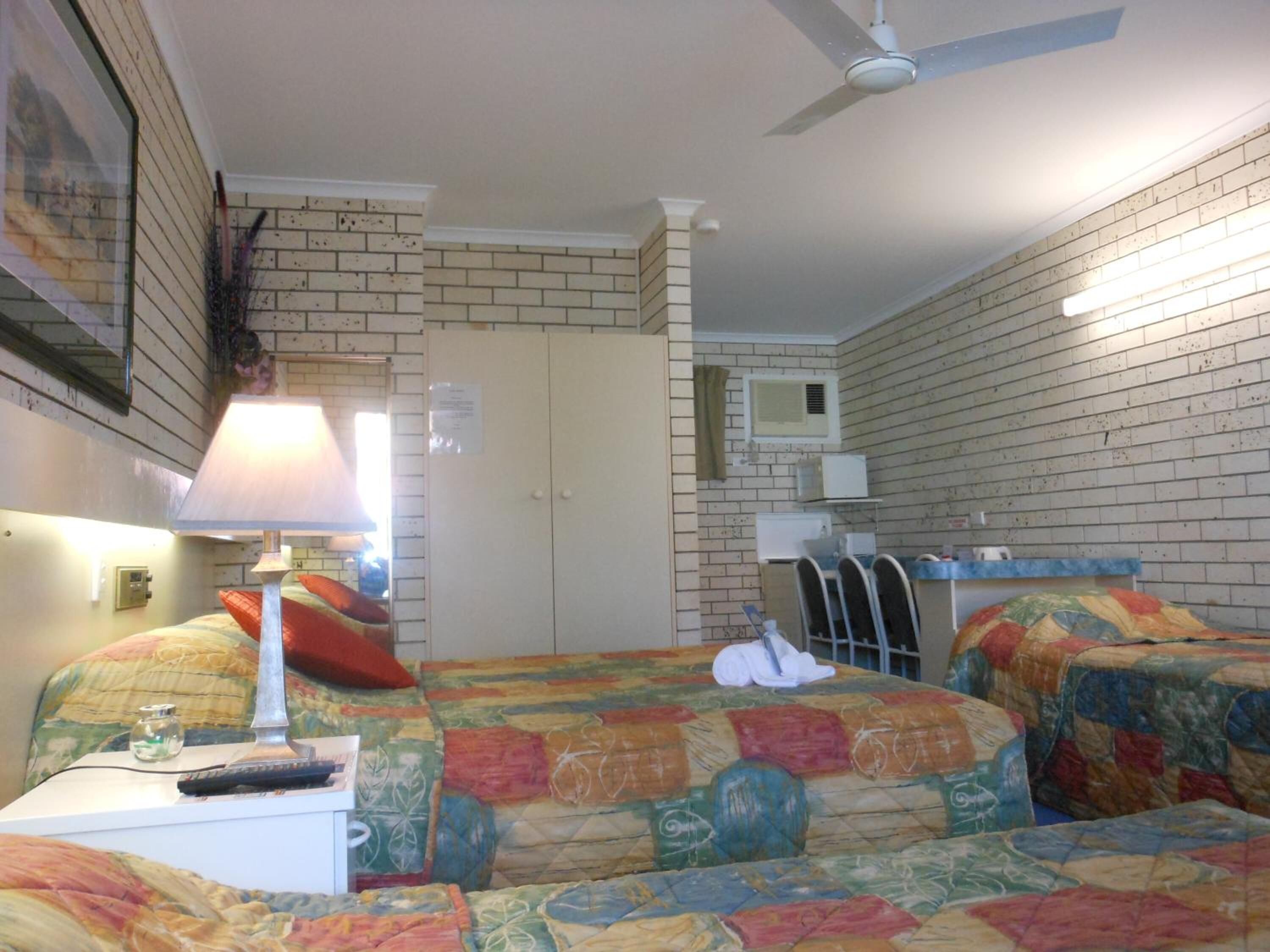 A hotel room with two beds, a desk with a lamp, a ceiling fan, a microwave, and a small window.