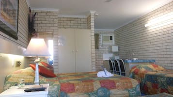 A hotel room with two beds, a desk with a lamp, a ceiling fan, a microwave, and a small window.