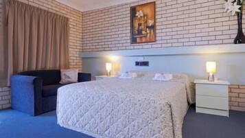 Une chambre d’hôtel avec un grand lit, un canapé, deux tables de chevet avec des lampes, un tableau au mur et un mur décoré d’un motif en briques.