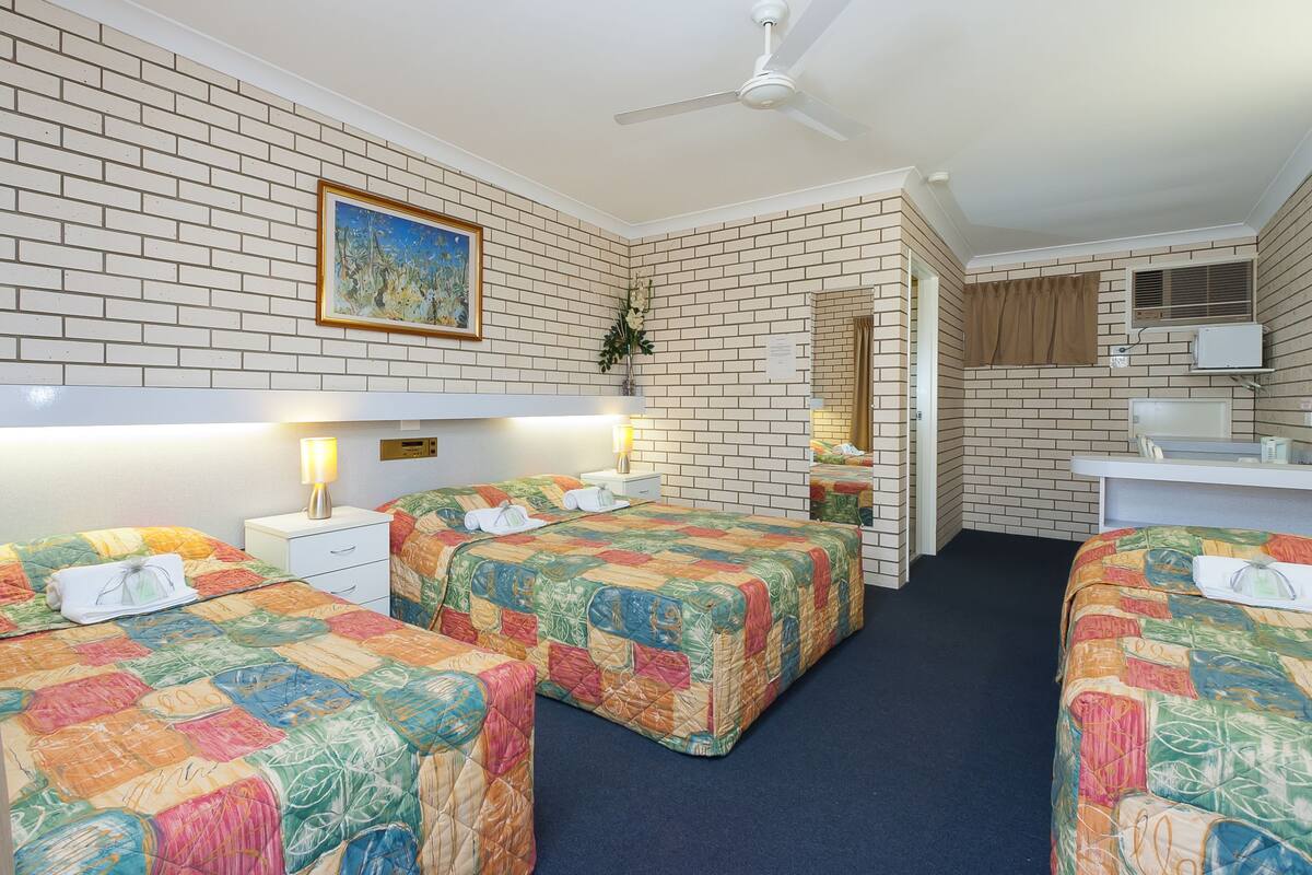 A hotel room with two beds, a desk, a mirror, a ceiling fan, and a brick-patterned wall.