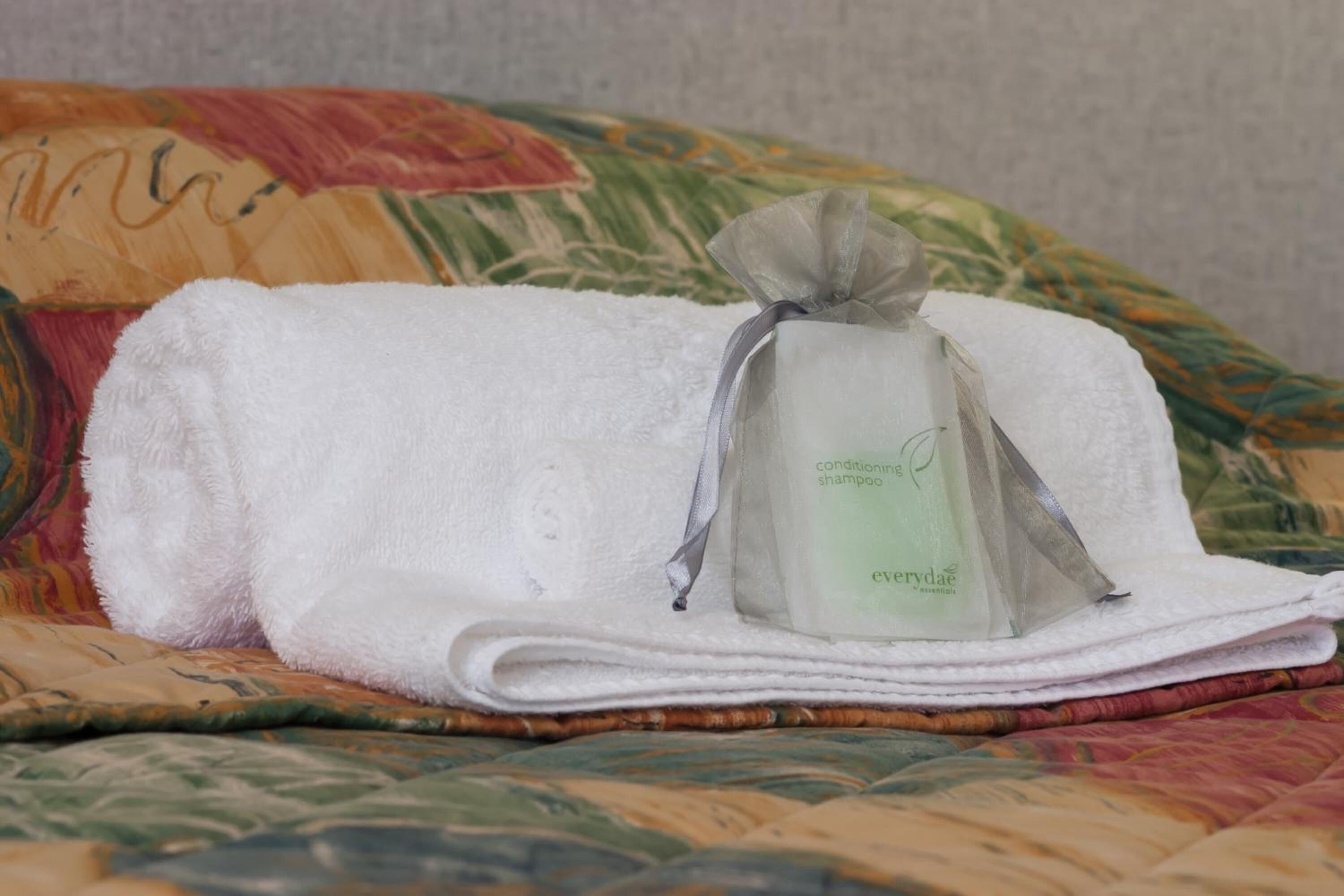 Ein ordentlich gefaltetes weißes Handtuch auf einem Bett mit einer farbenfrohen, gemusterten Bettdecke.