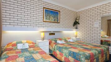 A hotel room with two beds, white brick walls, a painting, and a mirror.