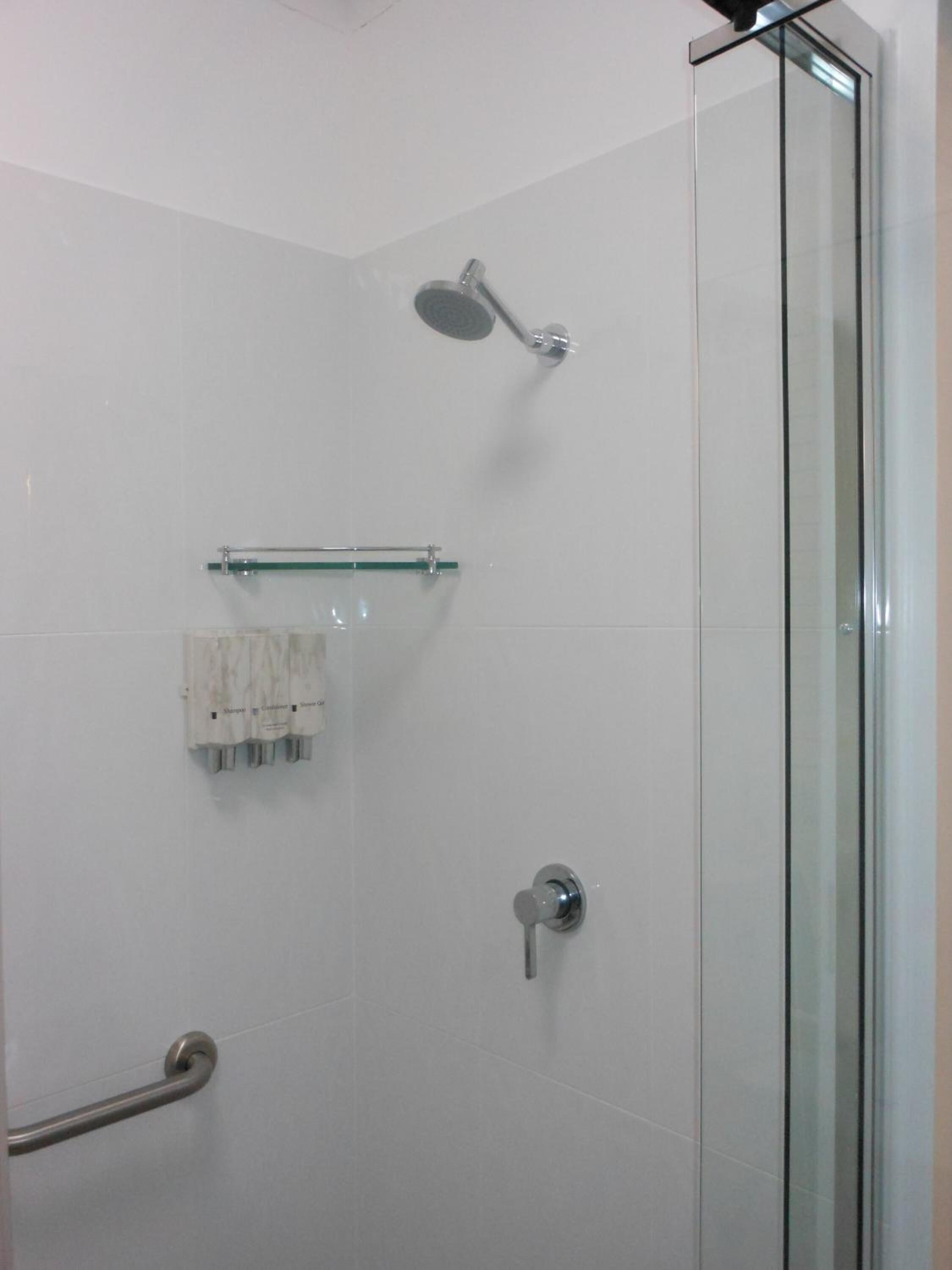 A modern shower with a glass door, a handheld showerhead, a towel rack, and a grab bar.