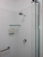 Ducha moderna con puerta de cristal, cabezal de ducha de mano, toallero y barra de apoyo.
