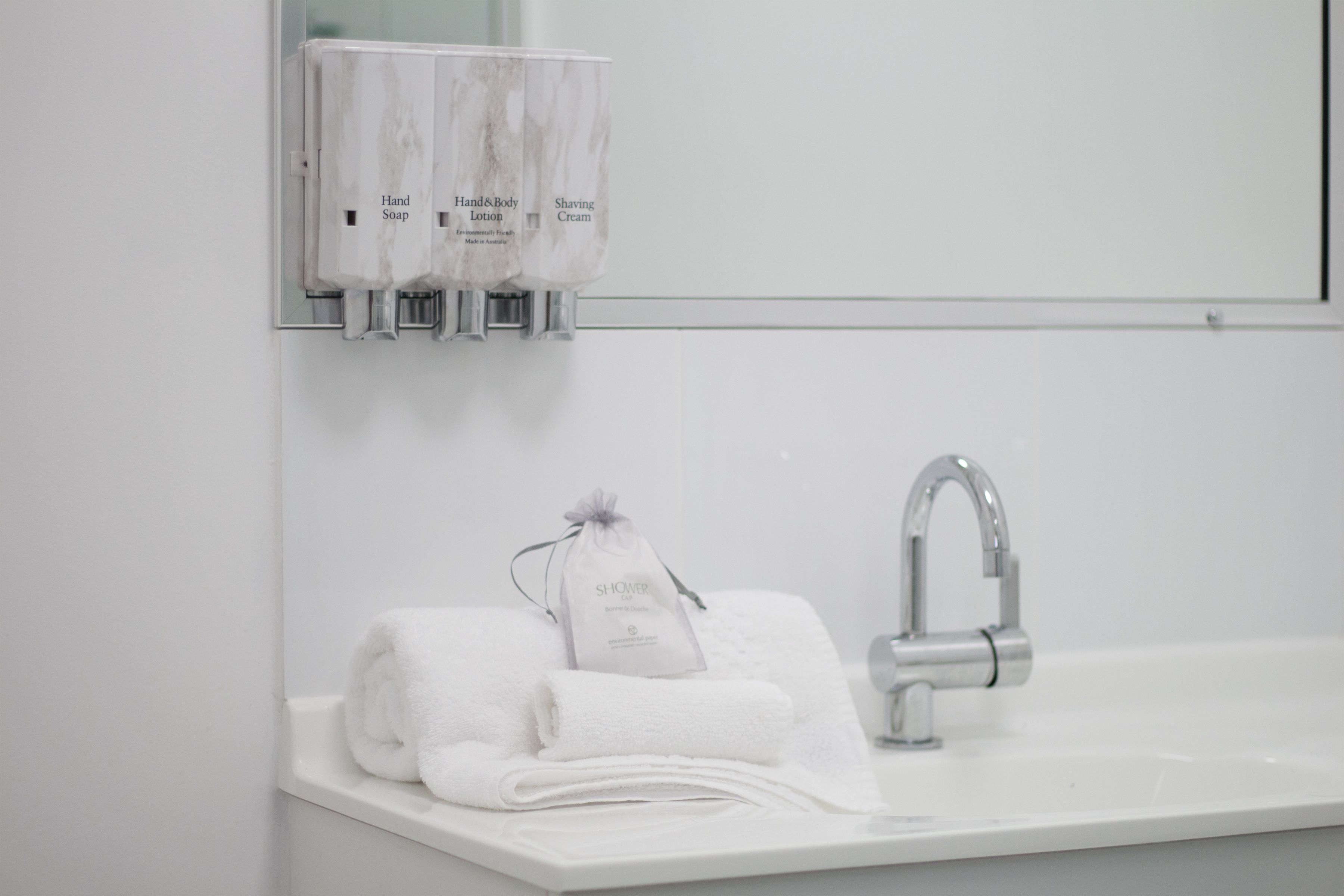 A bathroom with a white sink, a mirror, and a hand soap dispenser.