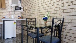 Una cocina compacta equipada con microondas, un refrigerador pequeño y una mesa de vidrio con sillas.